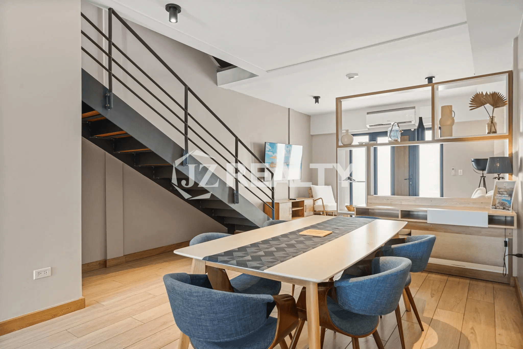 Dining area in Porta al Sole Unit 10 featuring a table with blue chairs and a modern, exposed metal and wood staircase leading upstairs.