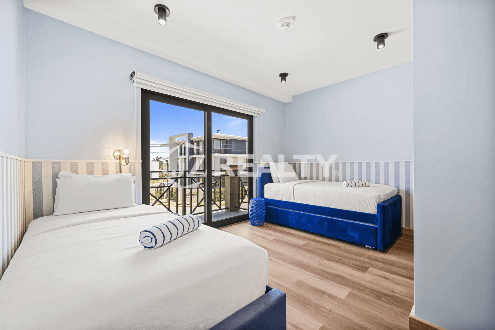 Guest bedroom in Porta al Sole Unit 10 with two twin beds featuring blue accents, a sliding glass door to a balcony, and light blue walls.