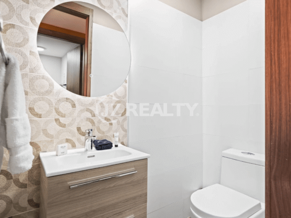Detail shot of the half bathroom in Porta al Sole Unit 10, featuring a wood vanity, round mirror, and decorative wall tile.