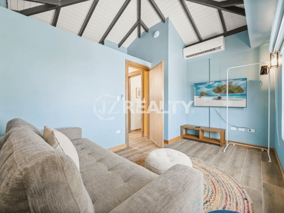 Spacious living area in Porta al Sole Unit 10 featuring a light blue accent wall, comfortable sofa, TV, and exposed vaulted ceiling beams.
