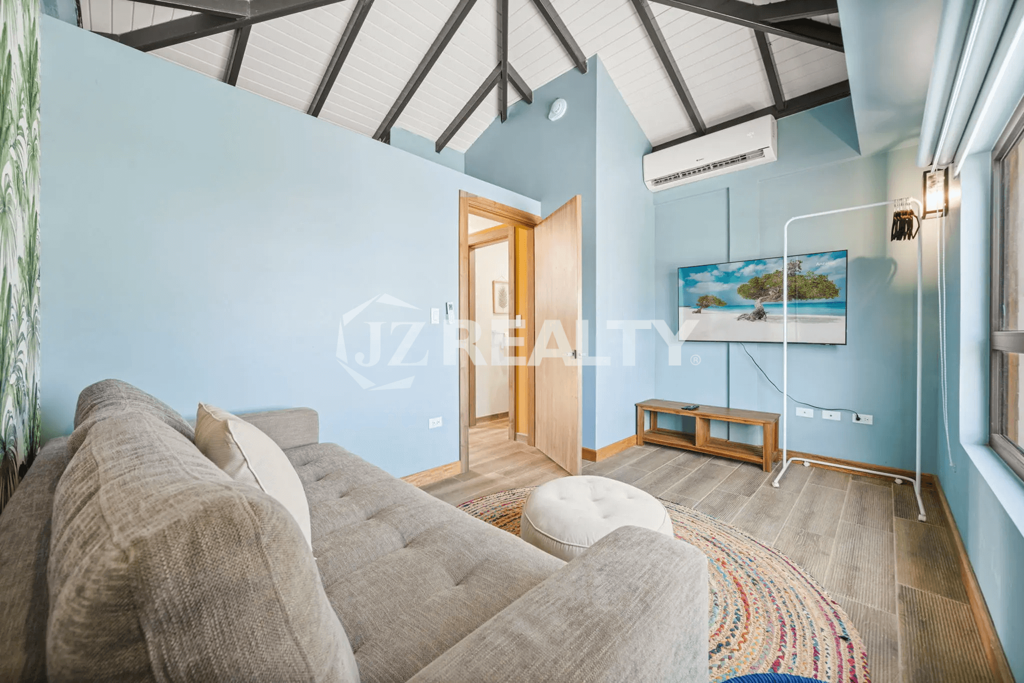 Spacious living area in Porta al Sole Unit 10 featuring a light blue accent wall, comfortable sofa, TV, and exposed vaulted ceiling beams.