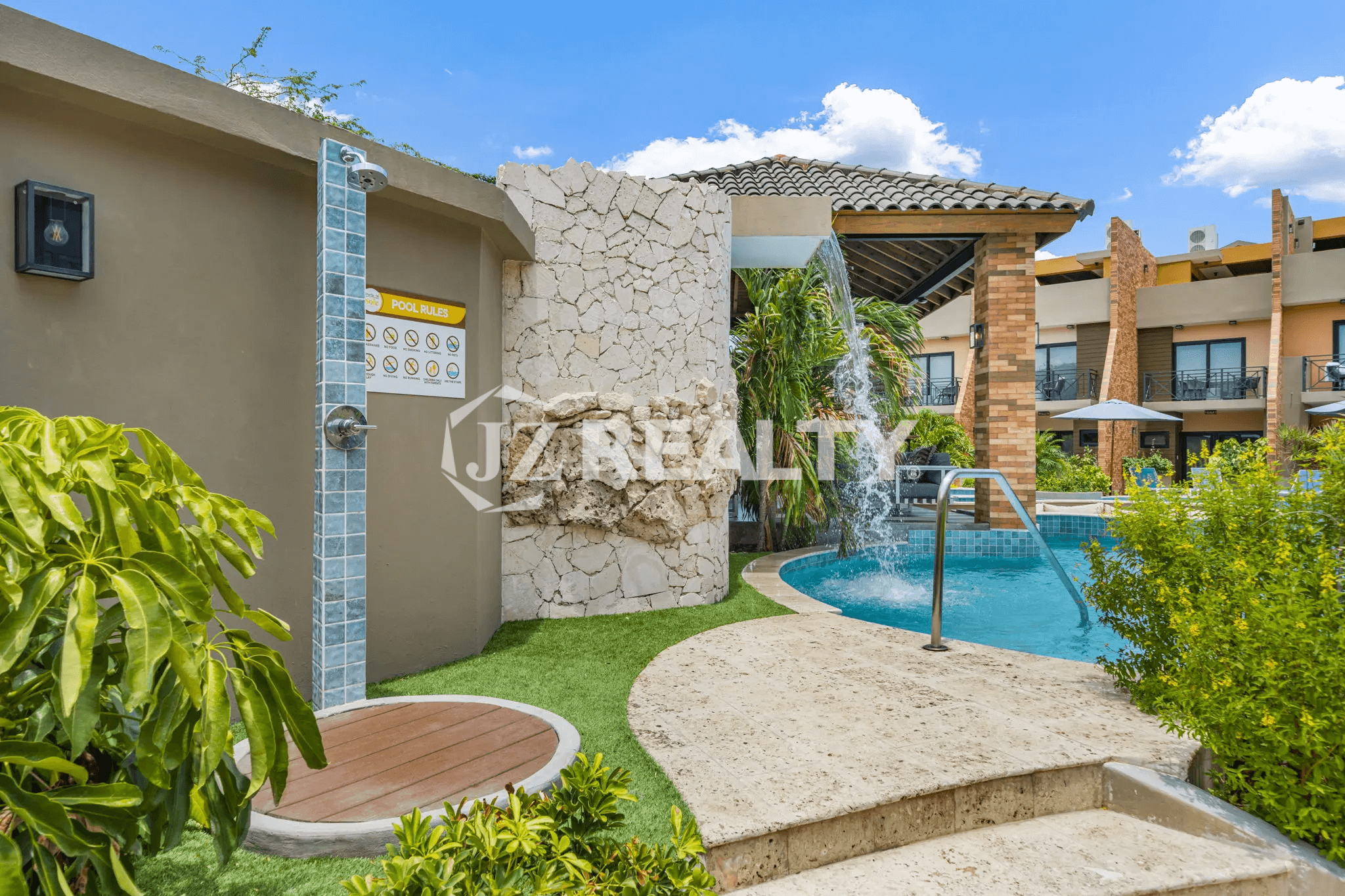 Detail of the community pool area at Porta al Sole, showing the outdoor shower station and the stone-clad waterfall feature.