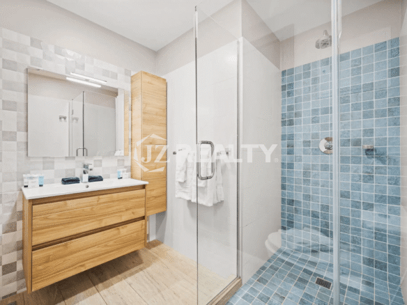 Stylish primary bathroom in Porta al Sole Unit 10 with wood vanity, glass shower enclosure, and blue mosaic tile shower floor and wall.