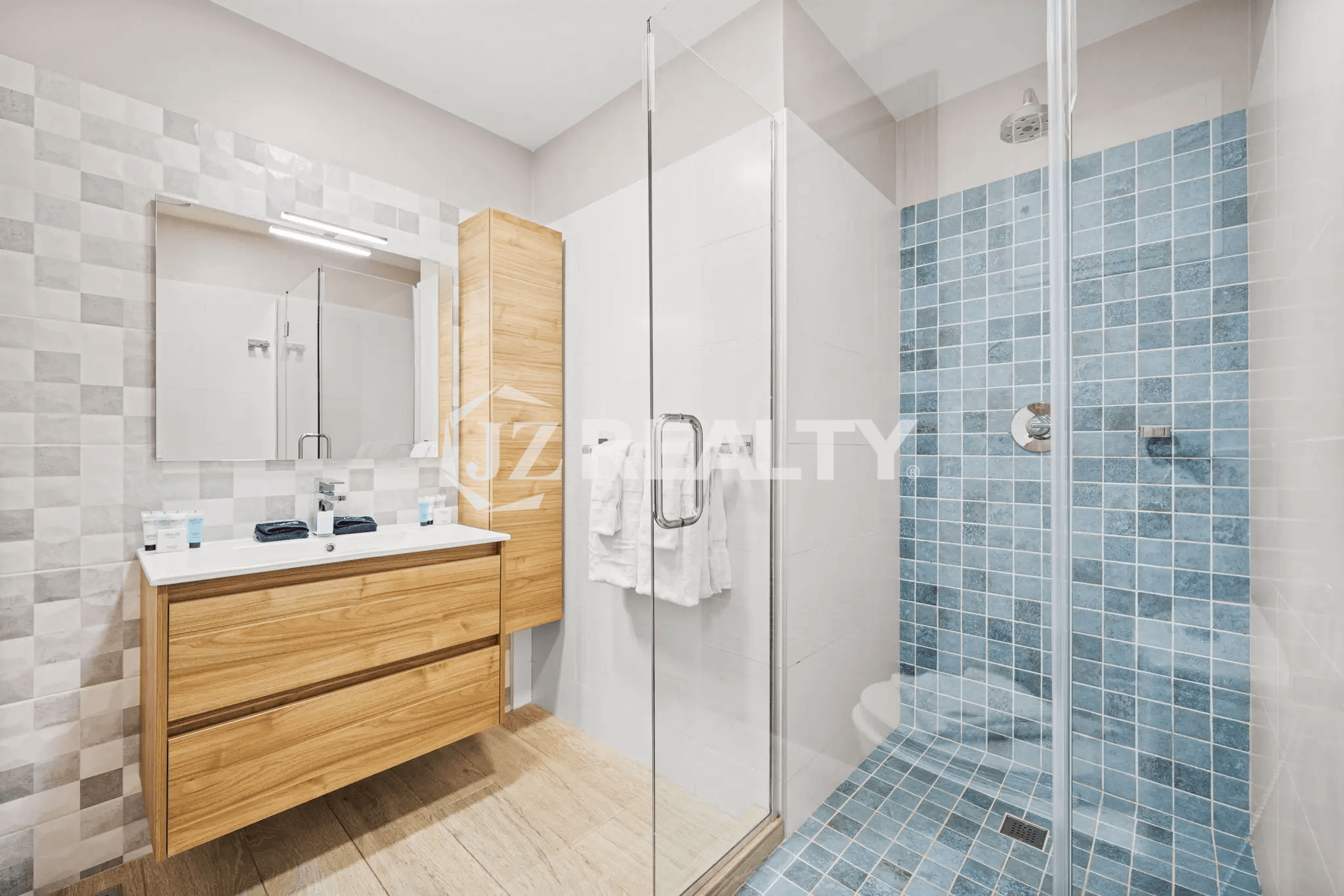 Stylish primary bathroom in Porta al Sole Unit 10 with wood vanity, glass shower enclosure, and blue mosaic tile shower floor and wall.