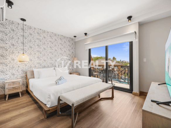 Spacious primary bedroom in Porta al Sole Unit 10 with a king bed, tropical wallpaper accent wall, and a sliding glass door opening to a private balcony.