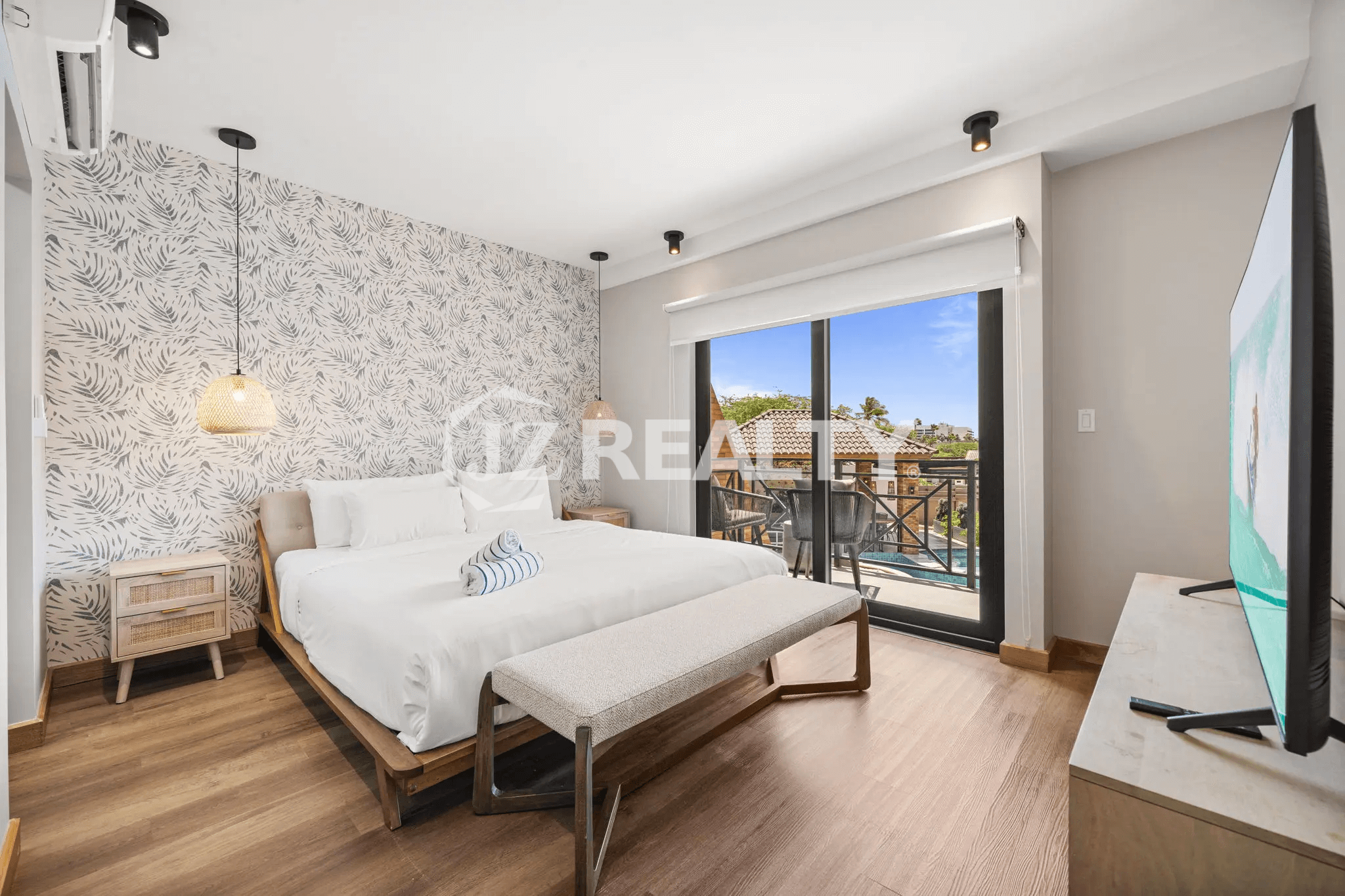Spacious primary bedroom in Porta al Sole Unit 10 with a king bed, tropical wallpaper accent wall, and a sliding glass door opening to a private balcony.