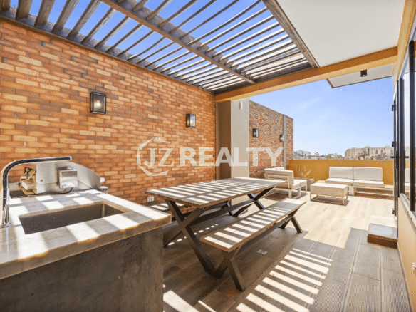 Rooftop terrace at Porta al Sole Unit 10 with a shaded pergola, brick wall, outdoor dining table, built-in BBQ/sink area, and lounge seating.