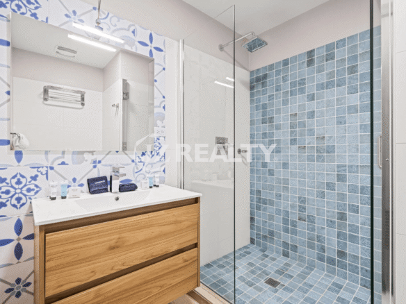 Guest bathroom in Porta al Sole Unit 10 featuring a blue and white patterned accent wall, wood vanity, and walk-in shower with blue square tiles.