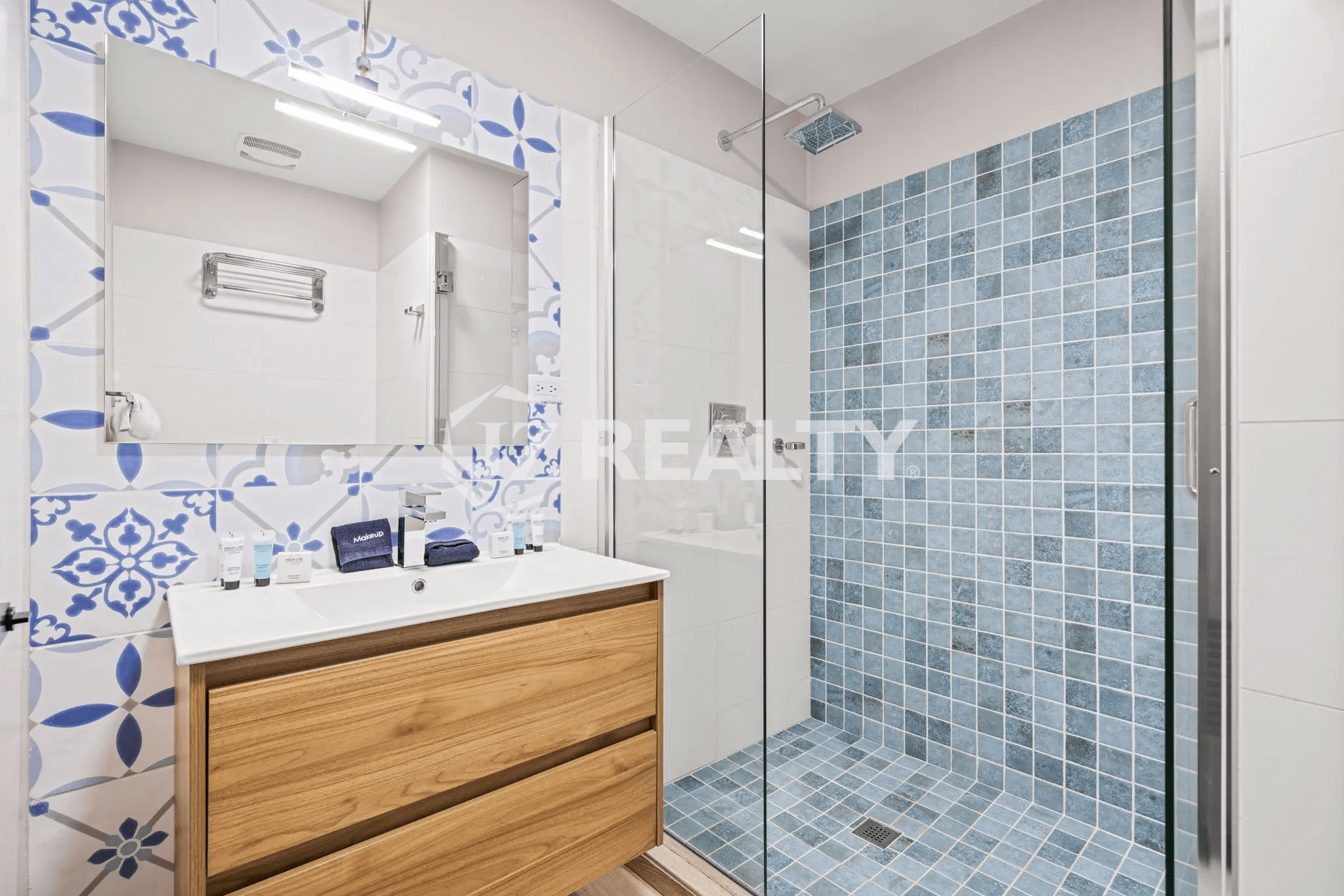 Guest bathroom in Porta al Sole Unit 10 featuring a blue and white patterned accent wall, wood vanity, and walk-in shower with blue square tiles.