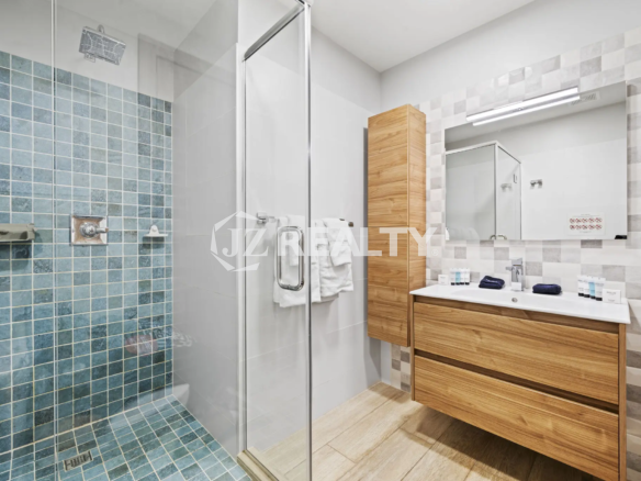 Porta al Sole Unit 11 spacious modern bathroom with a glass-enclosed shower featuring blue square mosaic tiles and a wooden double-drawer vanity.