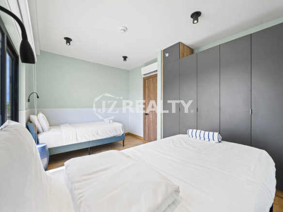 Porta al Sole Unit 11 modern bedroom featuring a light mint green wall, two beds with white linen, and large dark grey built-in wardrobes.
