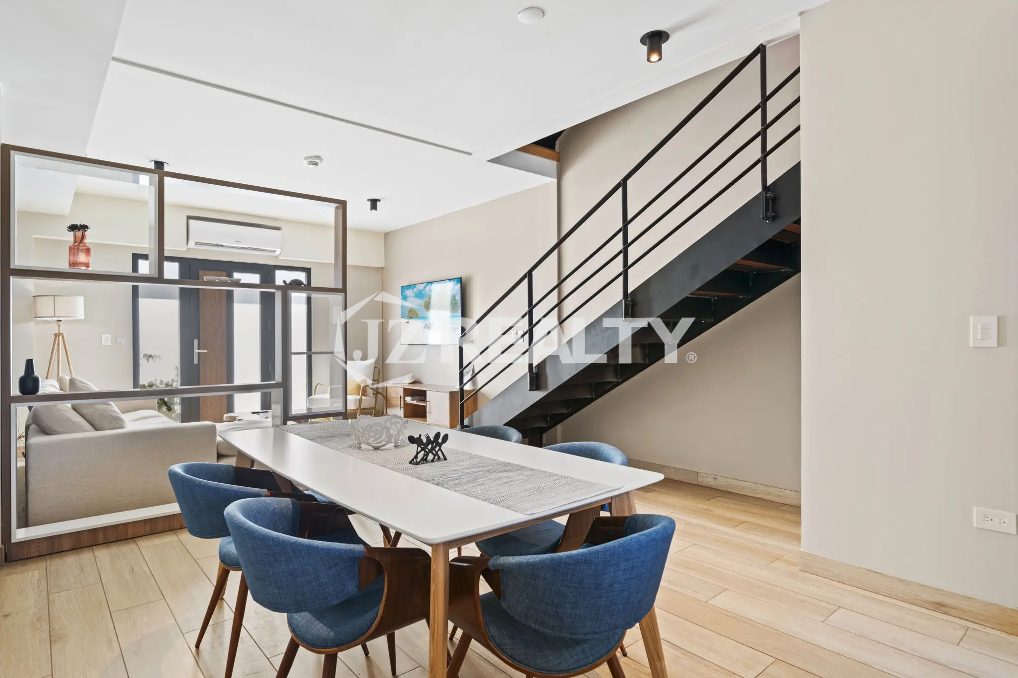 Porta al Sole Unit 11 open-plan dining area with a long white table, modern blue chairs, and a contemporary open-riser staircase with black metal railings.