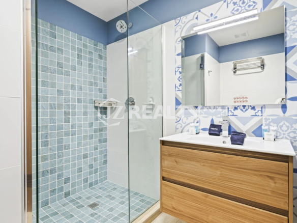 Porta al Sole Unit 11 en suite bathroom with a glass shower stall, blue and white patterned accent tiles, and a light wood vanity.