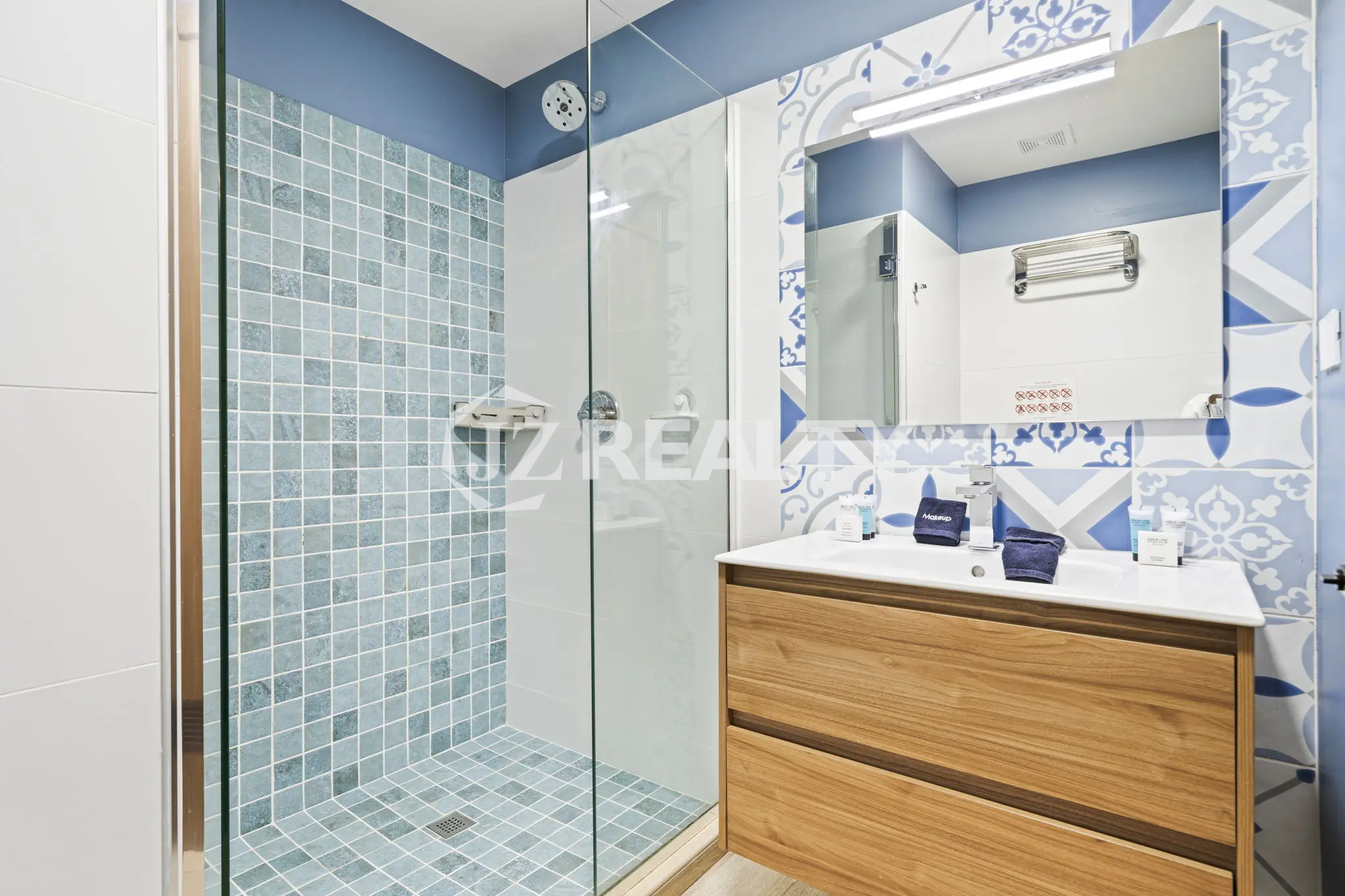 Porta al Sole Unit 11 en suite bathroom with a glass shower stall, blue and white patterned accent tiles, and a light wood vanity.
