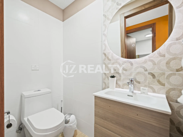 Porta al Sole Unit 11 small guest bathroom with white tile walls, a round mirror over a wood vanity, and a white toilet.