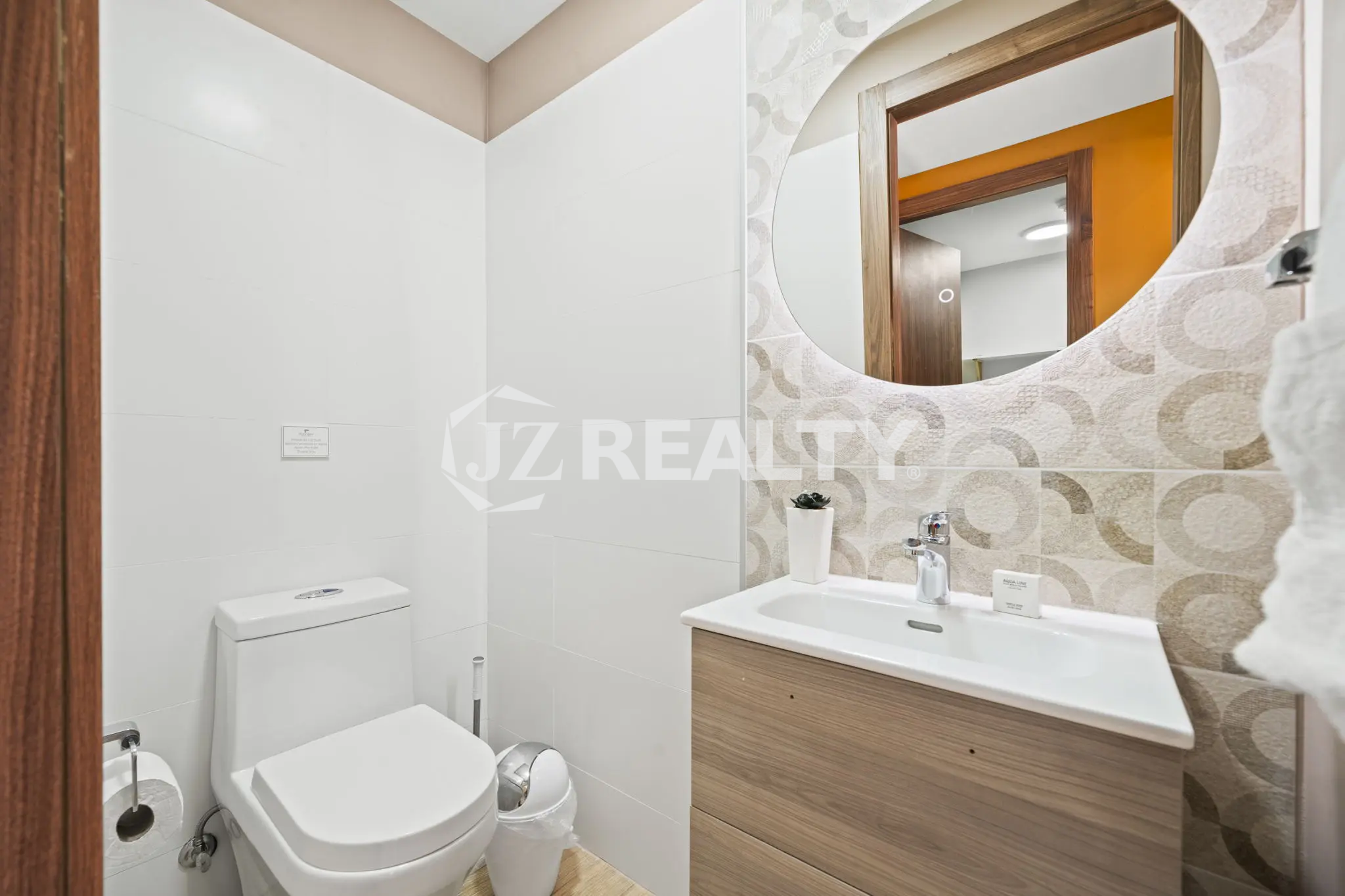 Porta al Sole Unit 11 small guest bathroom with white tile walls, a round mirror over a wood vanity, and a white toilet.