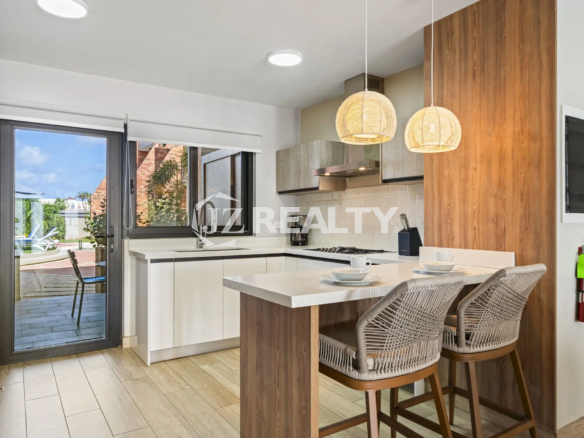 Porta al Sole Unit 11 modern kitchen with a white quartz countertop, breakfast bar seating, subway tile backsplash, and a sliding glass door to the patio.