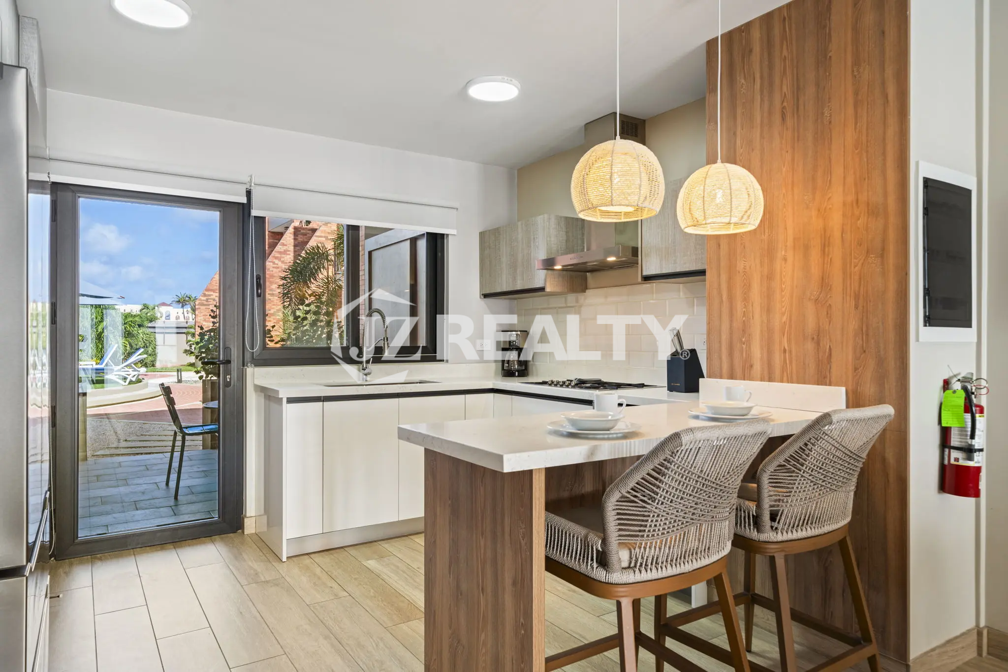 Porta al Sole Unit 11 modern kitchen with a white quartz countertop, breakfast bar seating, subway tile backsplash, and a sliding glass door to the patio.