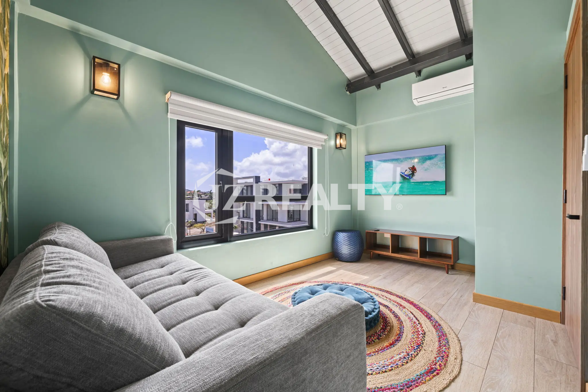 Porta al Sole Unit 11 bright living area with mint green walls, a grey sofa/daybed, wall-mounted TV, and an air conditioning unit.