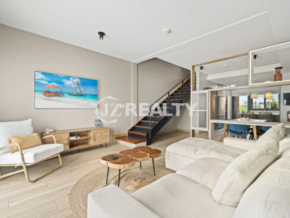 Porta al Sole Unit 11 bright living room with a large white sectional sofa, wood media console, natural fiber rug, and view of the interior staircase.