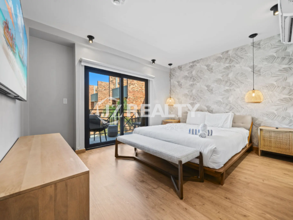 Porta al Sole Unit 11 master bedroom with a king-sized bed, decorative tropical wallpaper accent wall, wood flooring, and glass doors leading to a private balcony.