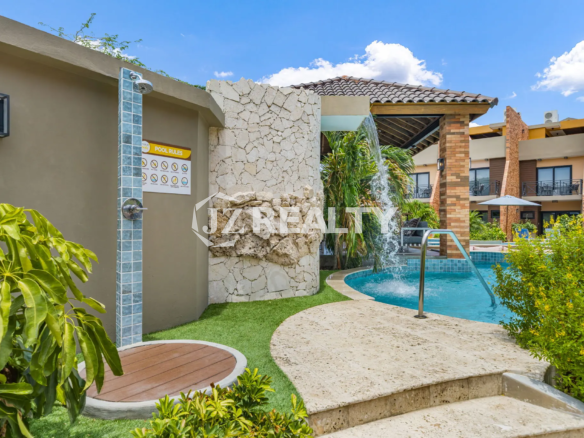 Porta al Sole Unit 11 outdoor shower station next to the pool, featuring a stone rock wall, wood-slat circular base, and pool rules sign.