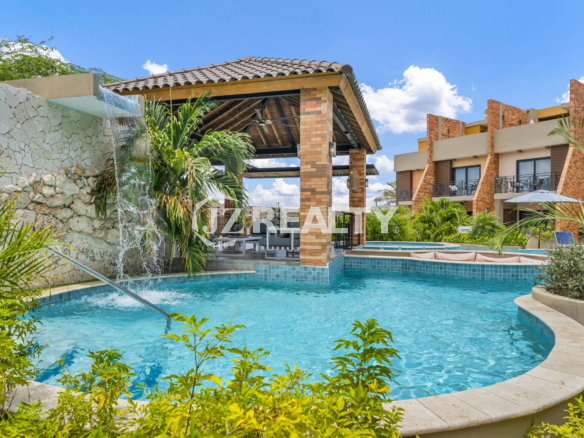 Porta al Sole Unit 11 community pool area with a decorative rock waterfall, covered lounge gazebo, and integrated shallow spa/jacuzzi area.