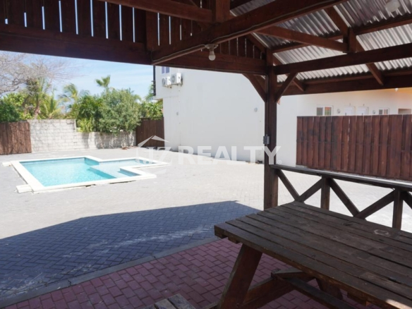 Covered patio gazebo with wooden picnic table overlooking the pool in an Aruba apartment complex.