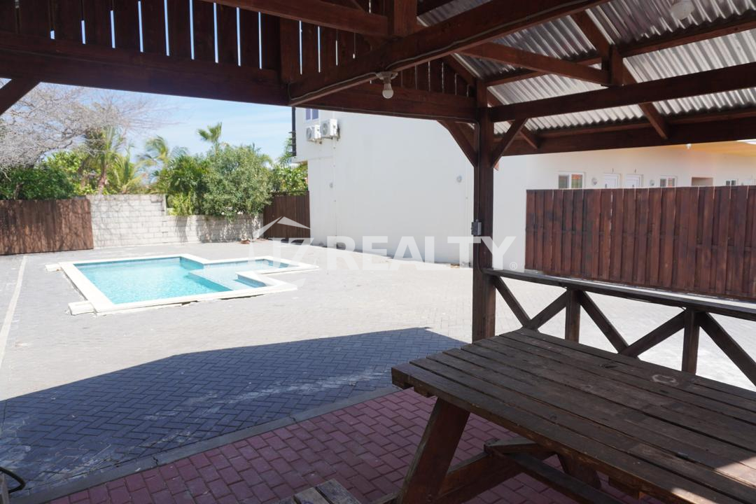 Covered patio gazebo with wooden picnic table overlooking the pool in an Aruba apartment complex.