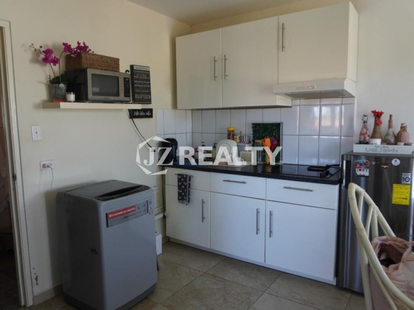 Compact kitchenette with cabinets, sink, washing machine, and refrigerator in an Aruba apartment.