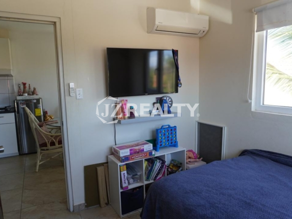Bedroom with wall-mounted TV, air conditioner, shelving, and window in an Aruba apartment.