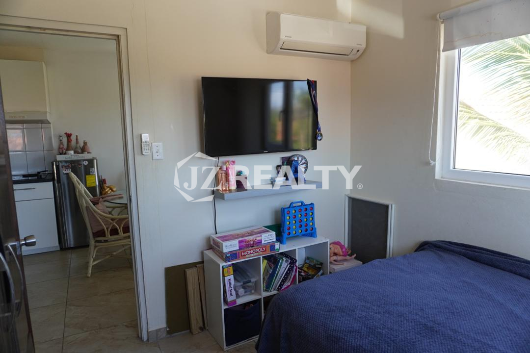 Bedroom with wall-mounted TV, air conditioner, shelving, and window in an Aruba apartment.