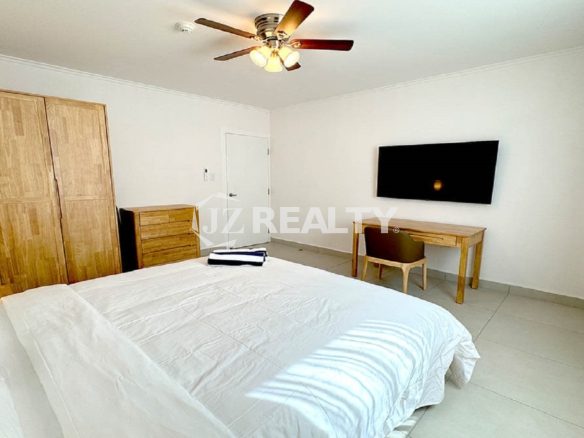 Spacious bedroom with a king bed, wooden furniture, and a wall-mounted TV.