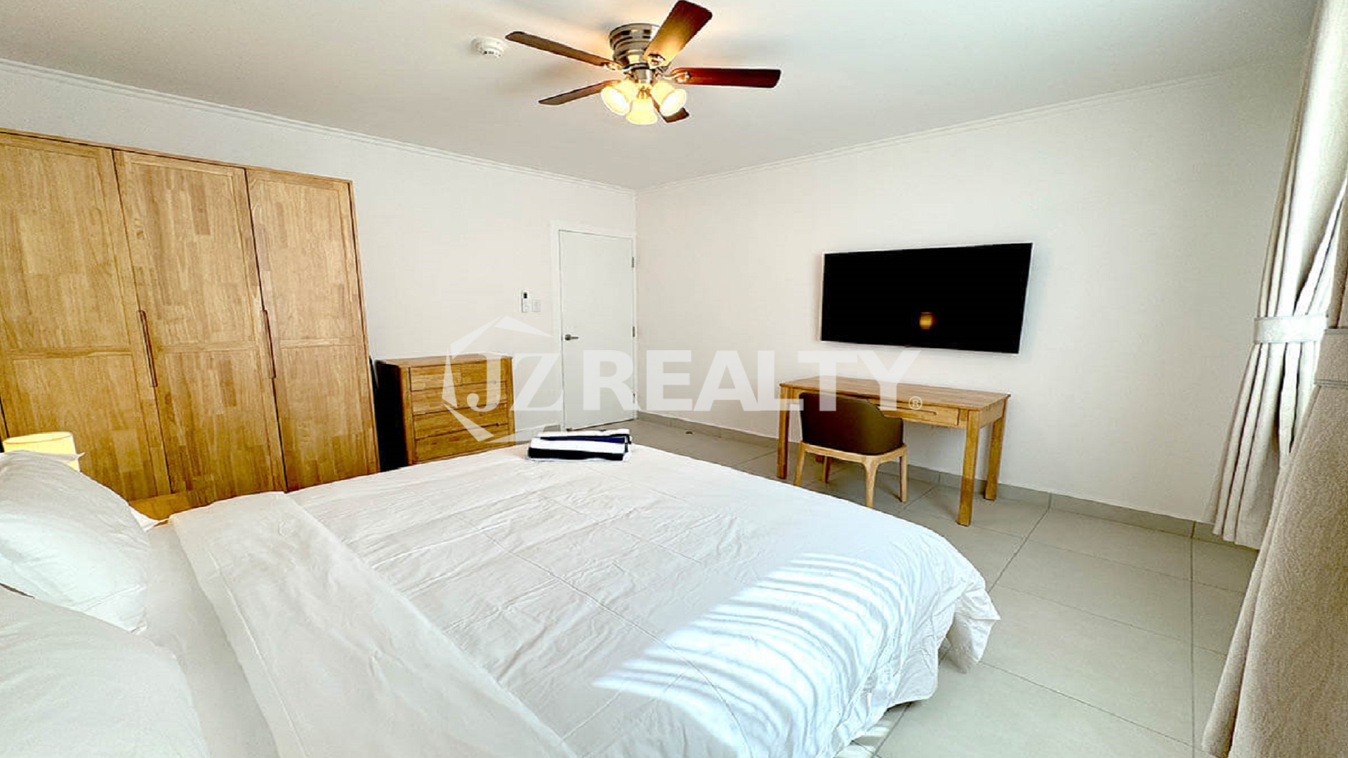 Spacious bedroom with a king bed, wooden furniture, and a wall-mounted TV.