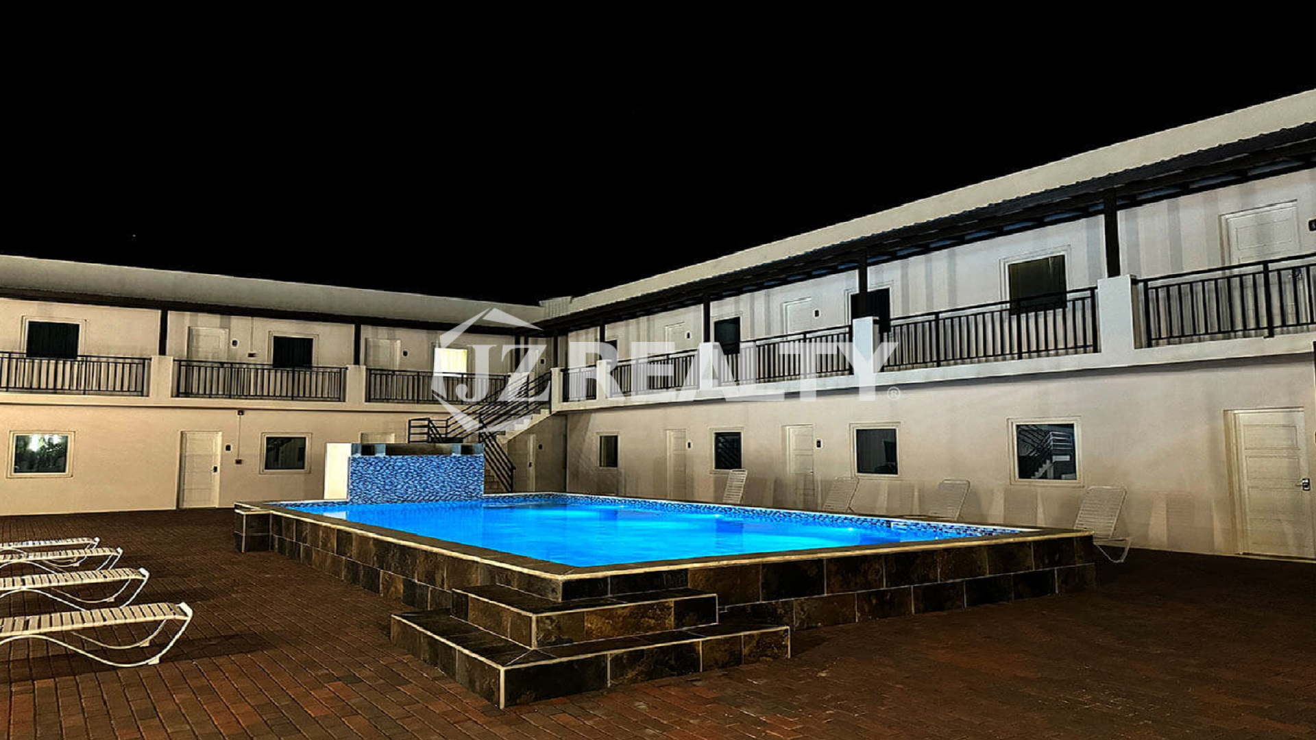 Night view of the courtyard pool and surrounding two-story buildings.