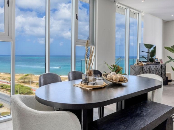Dining area in Reef Residences PHA penthouse beside large ocean view windows in Eagle Beach Aruba
