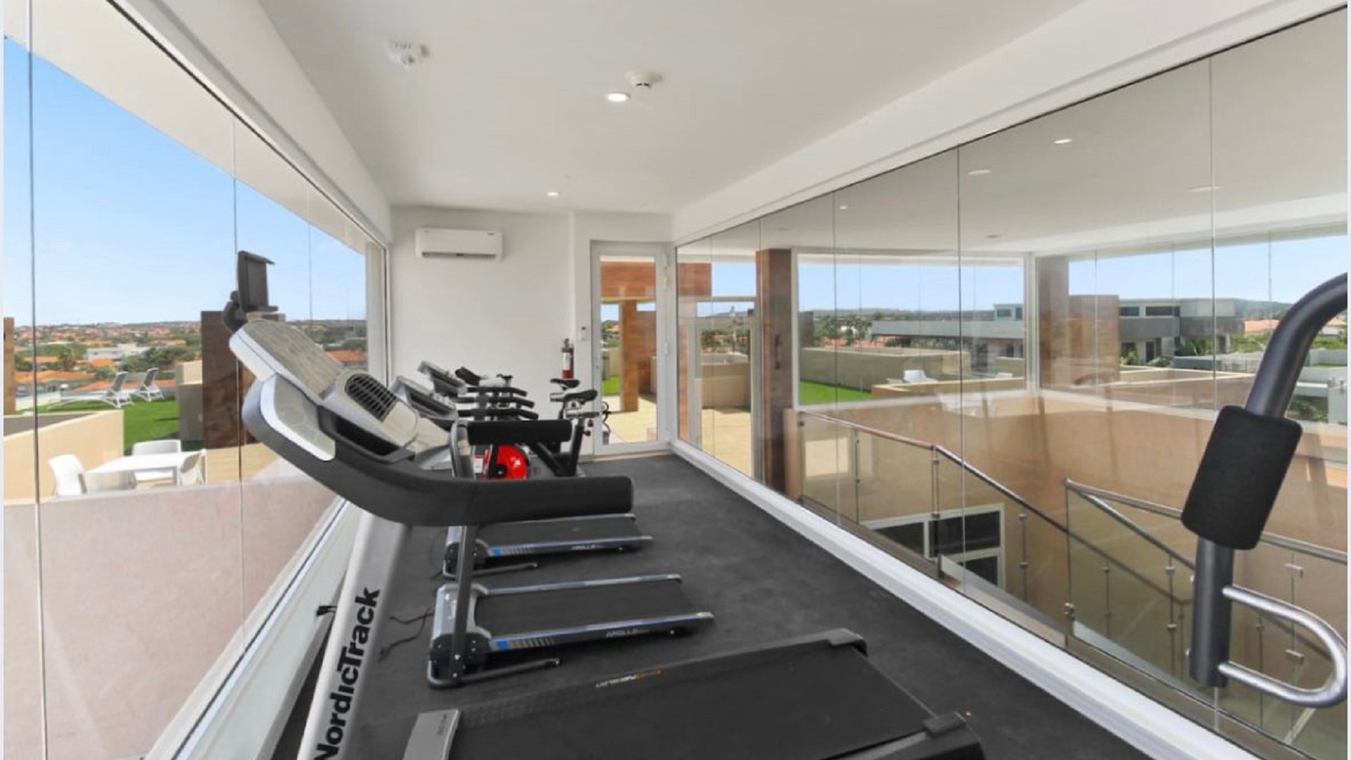 Fitness room at the 2-Bedroom Oasis at Aracari in Aruba with treadmills, exercise equipment, and large glass windows.