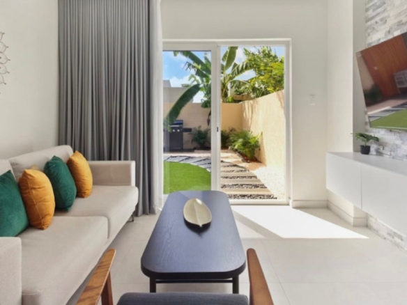 Bright living room at the 2-Bedroom Oasis at Aracari in Aruba with sofa, coffee table, wall-mounted TV, and sliding doors leading to the patio.