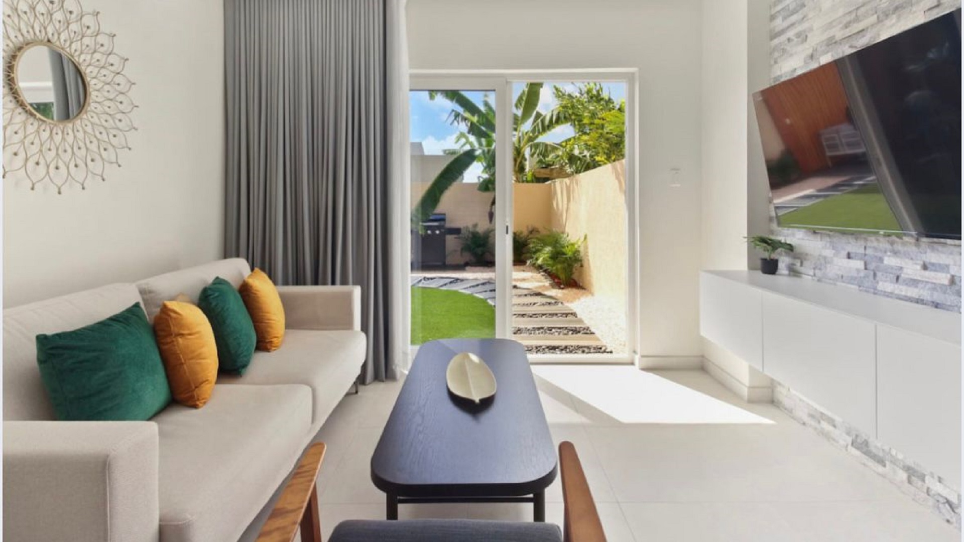 Bright living room at the 2-Bedroom Oasis at Aracari in Aruba with sofa, coffee table, wall-mounted TV, and sliding doors leading to the patio.