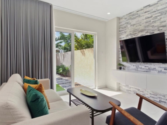 Living room at the 2-Bedroom Oasis at Aracari in Aruba with stone accent wall, wall-mounted TV, and patio access.
