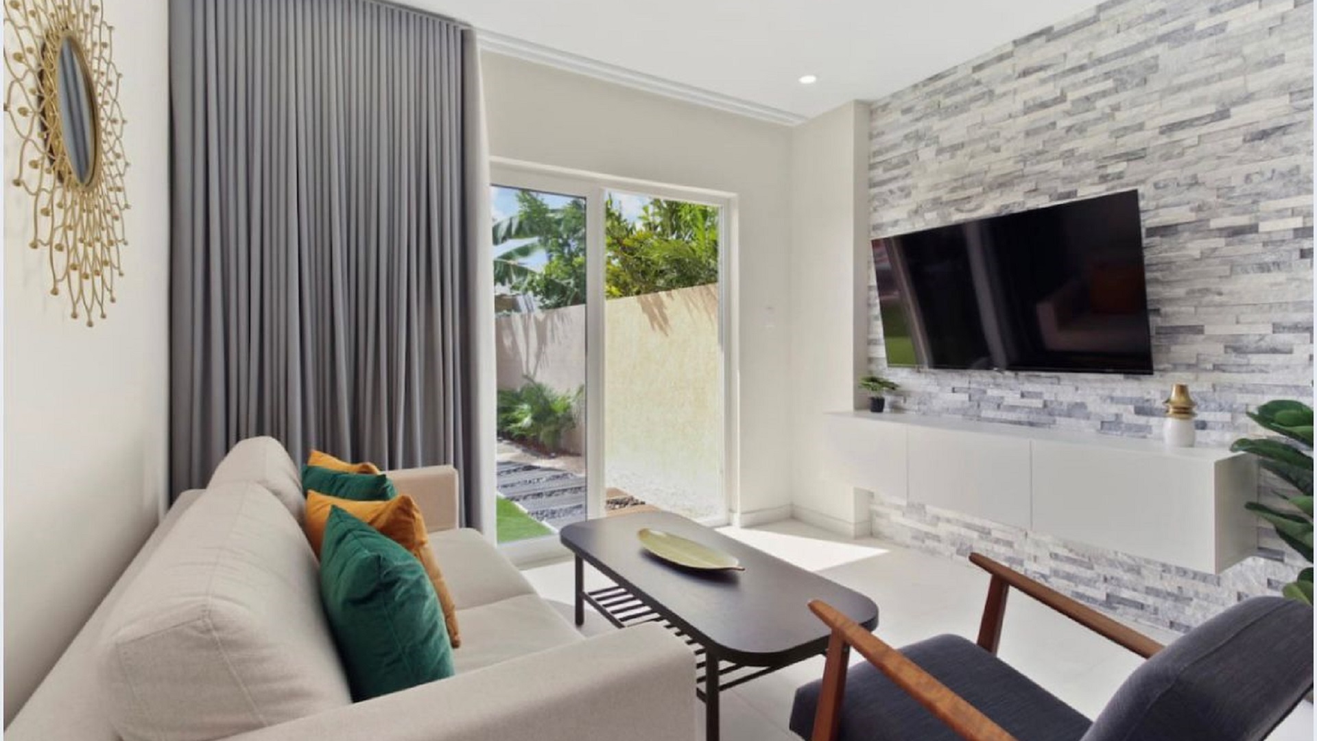 Living room at the 2-Bedroom Oasis at Aracari in Aruba with stone accent wall, wall-mounted TV, and patio access.