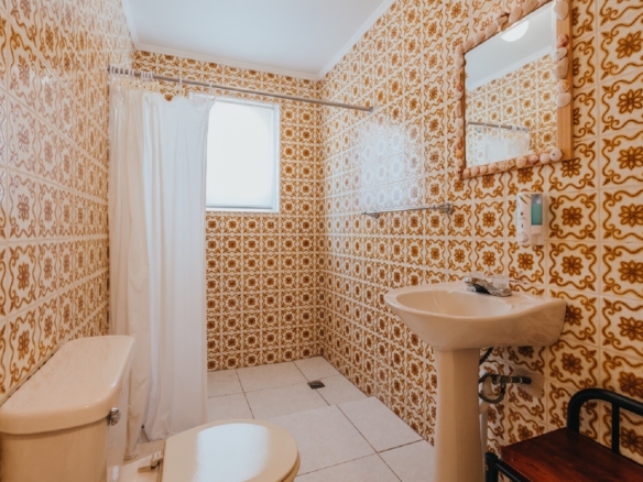 Bathroom with patterned tile walls inside one of the 7 studio apartments in Aruba featuring a shower curtain, pedestal sink, and tiled interior