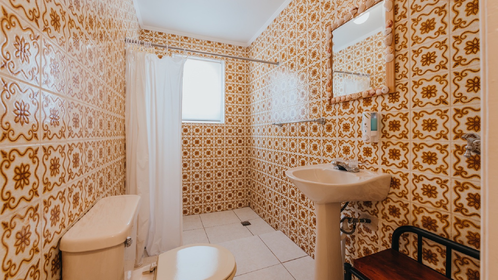 Bathroom with patterned tile walls inside one of the 7 studio apartments in Aruba featuring a shower curtain, pedestal sink, and tiled interior