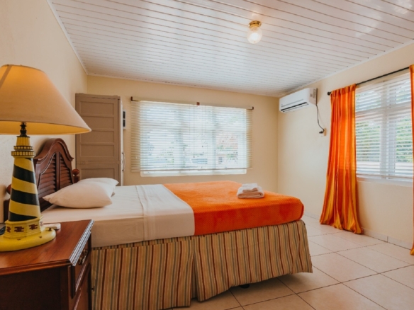 Alternate bedroom view in the 7 studio apartments in Aruba showing orange bedding, air conditioning, and large windows