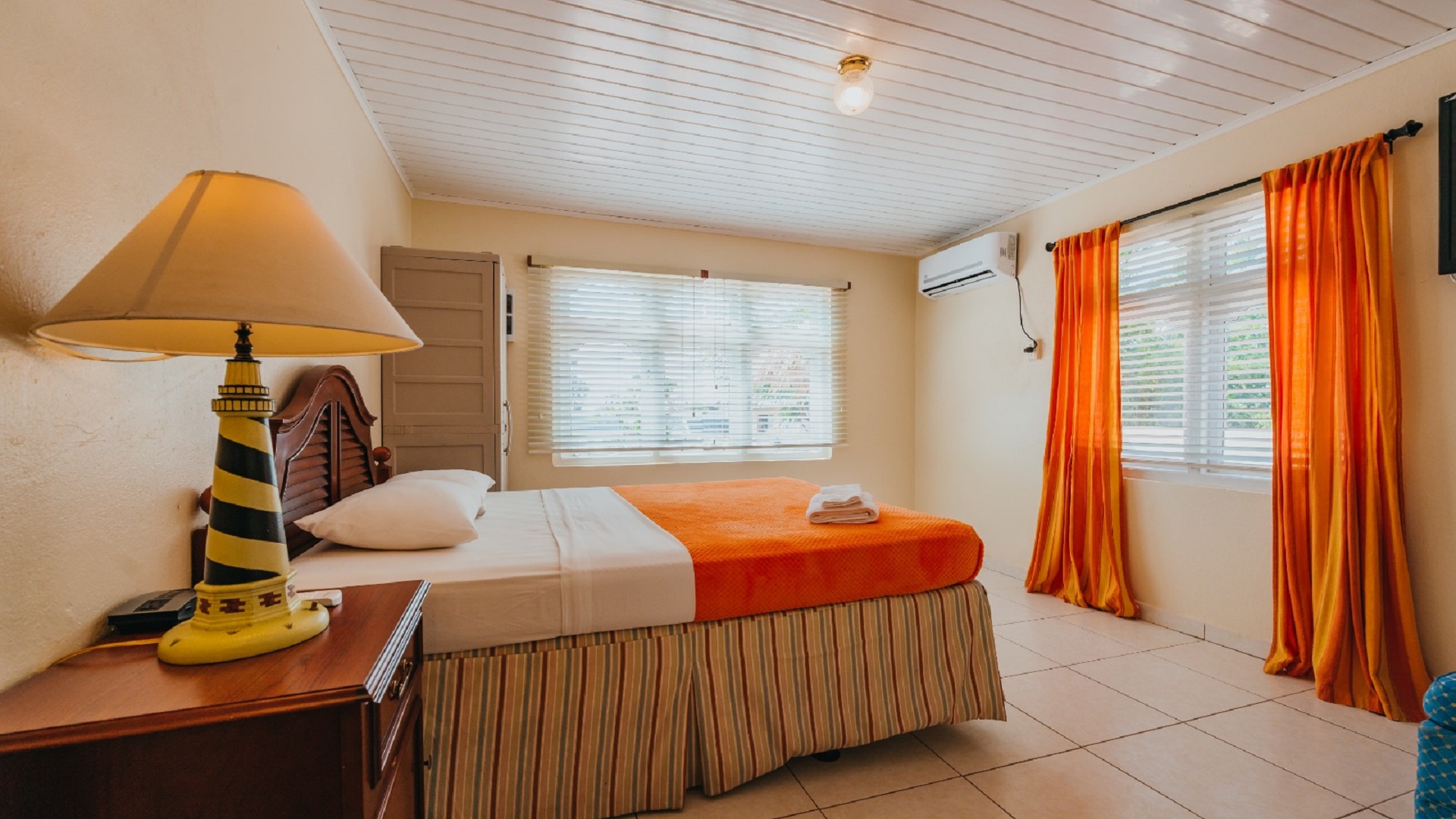 Alternate bedroom view in the 7 studio apartments in Aruba showing orange bedding, air conditioning, and large windows