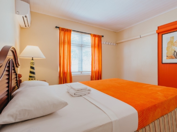 Bedroom inside the 7 studio apartments in Aruba featuring orange bedding, bedside table, curtains, and tiled flooring