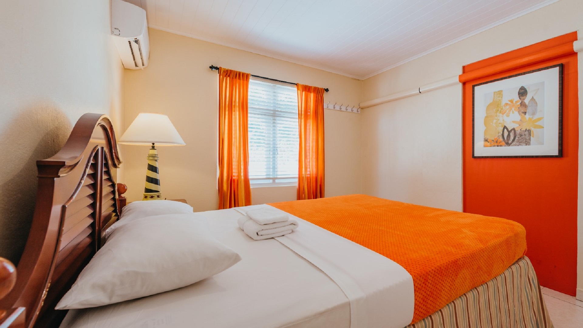 Bedroom inside the 7 studio apartments in Aruba featuring orange bedding, bedside table, curtains, and tiled flooring