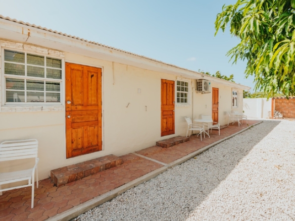 Exterior walkway of the 7 studio apartments in Aruba showing unit entrances, outdoor seating, and gravel courtyard