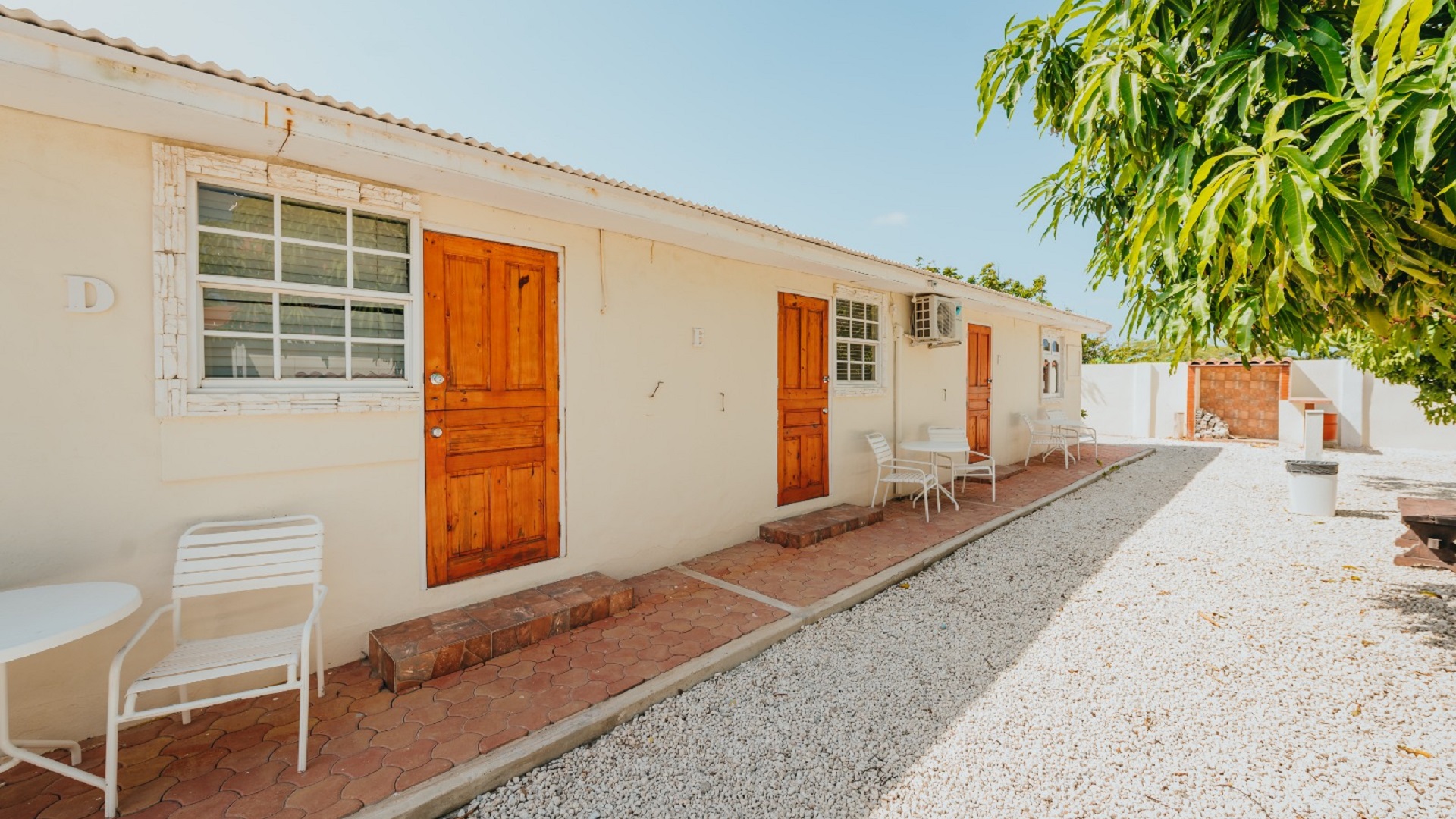 Exterior walkway of the 7 studio apartments in Aruba showing unit entrances, outdoor seating, and gravel courtyard