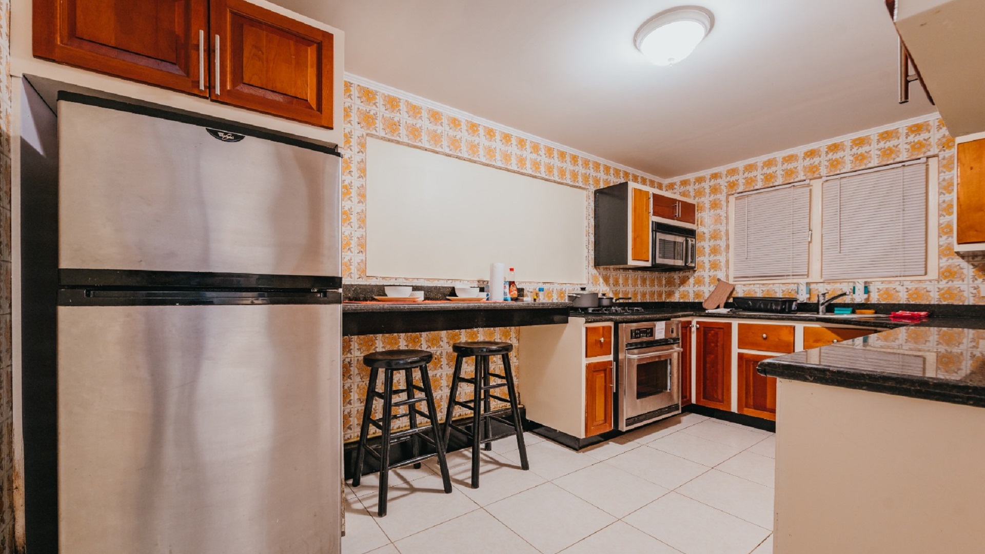 Kitchen inside the 7 studio apartments in Aruba with stainless steel refrigerator, bar seating, tiled flooring, and wood cabinetry